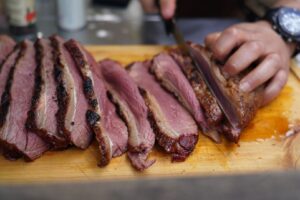 Skivat rosastekt kött med krispig yta på en skärbräda
